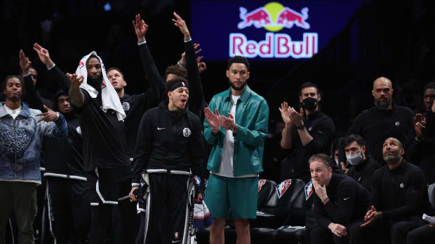 Apr 12, 2022; Brooklyn, New York, USA; Brooklyn Nets guard Ben Simmons (green jacket) reacts with center Andre Drummond (0) and guard Seth Curry (30) during the first half against the Cleveland Cavaliers at Barclays Center. Mandatory Credit: Vincent Carchietta-USA TODAY Sports